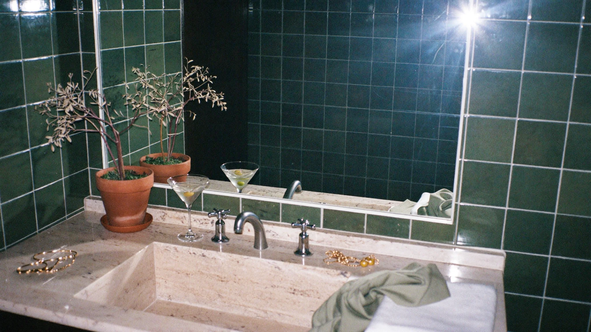 A dark green-tiled bathroom vanity with olive trees, martinis with olives and gold jewelry; the Rebuild blend details are etched into the mirror.